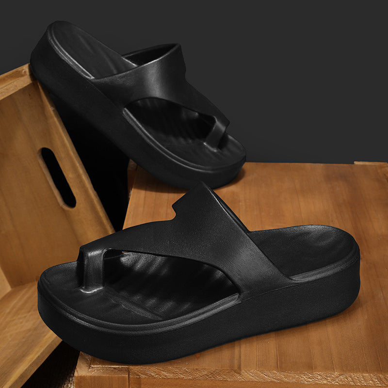 Chanclas de playa para mujer en color negro de material EVA con suela gruesa y diseño ligero sobre madera.
