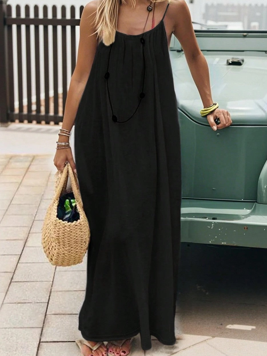 Vestido largo negro de tirantes ajustables y corte holgado con bolso de rafia en un estilo casual urbano.