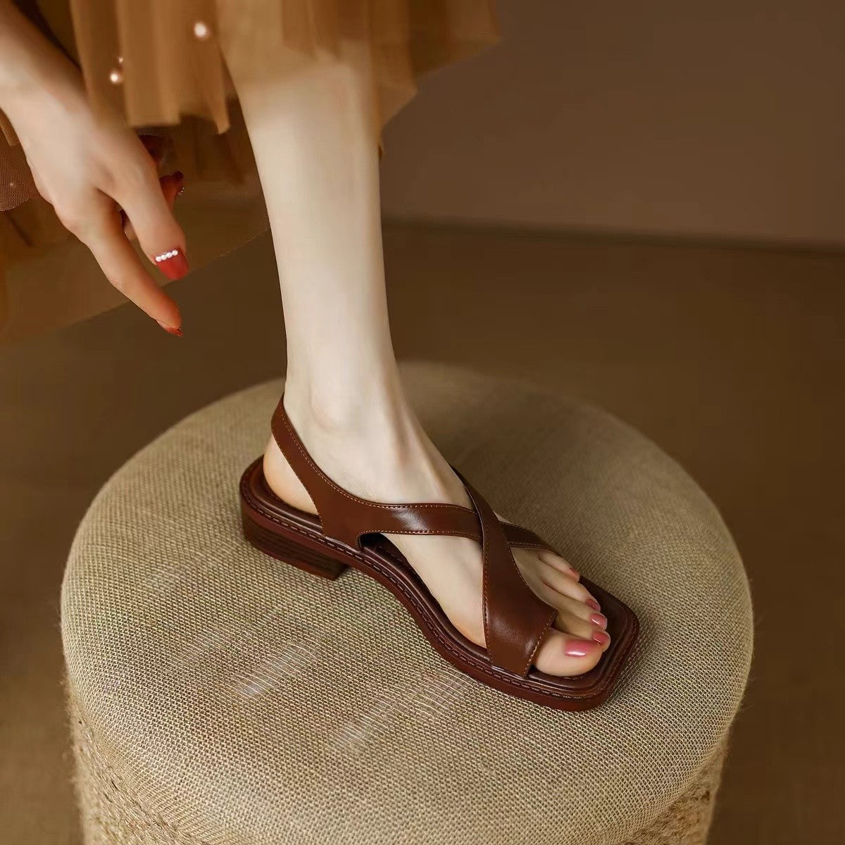Sandalias retro francesas de piel marrón con punta cuadrada y diseño de dedo para mujer sobre taburete.