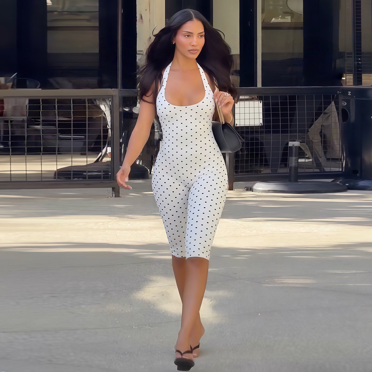 Modelo con mono ajustado blanco de puntos negros, escote halter y espalda descubierta para un look urbano.